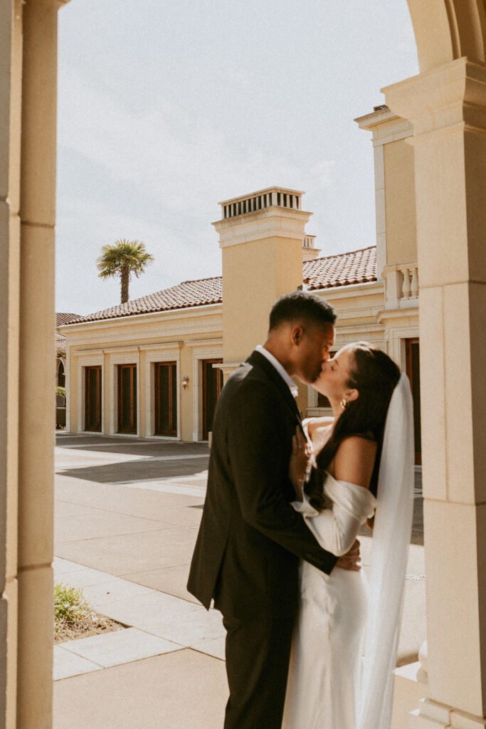 A bride and groom are kissing in front of a building.