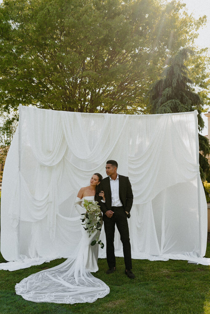 A bride and groom are posing for a picture in front of a white curtain.