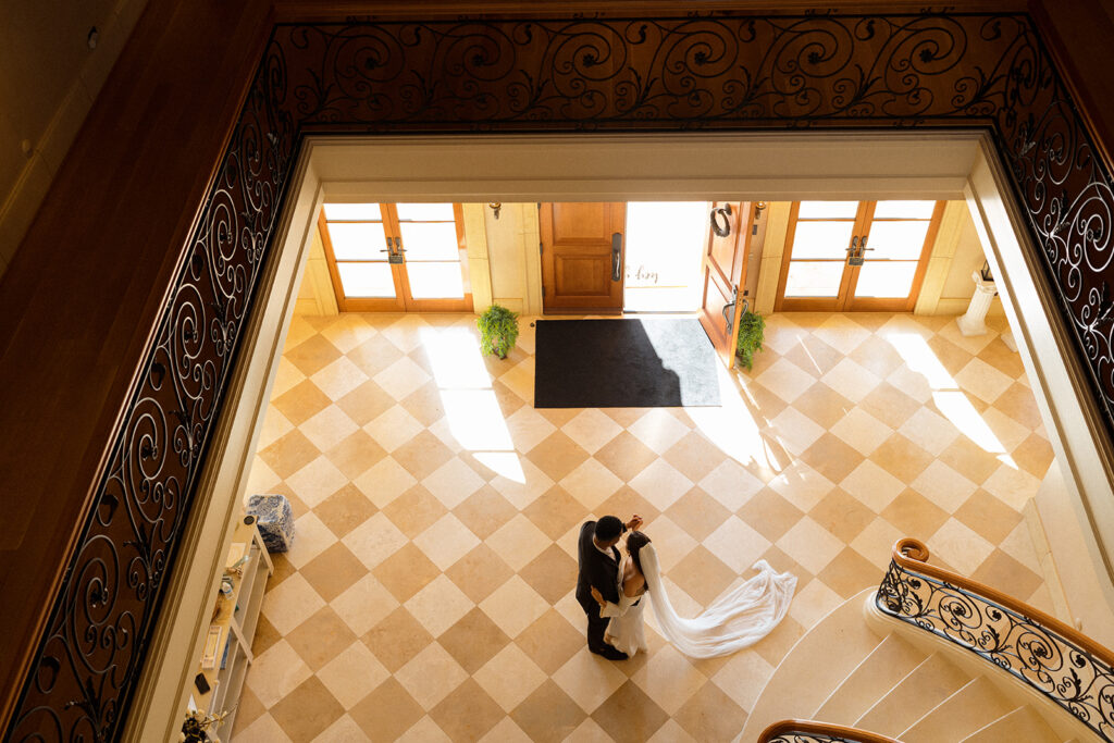 An aerial view of a bride and groom kissing in a hallway.