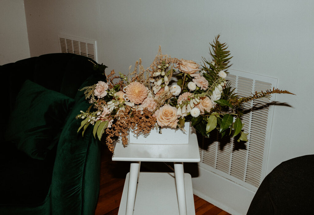 A vase of flowers is sitting on a white stool in a living room.