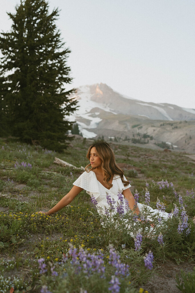 A woman in a white dress is sitting in a field of purple flowers.