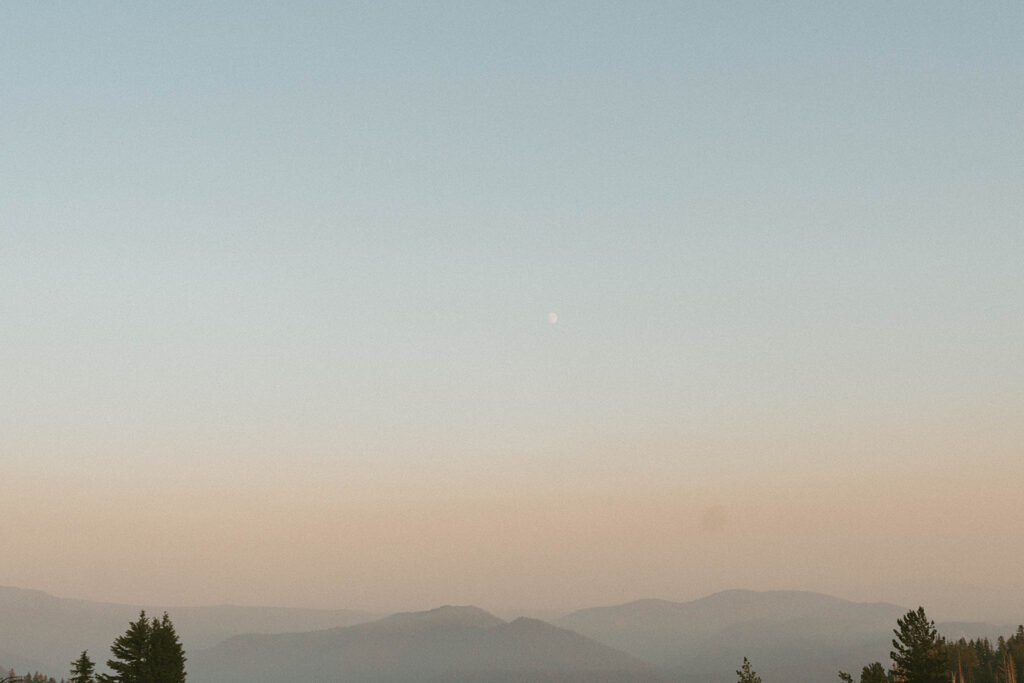 A view of a mountain range with trees in the foreground and a blue sky in the background.