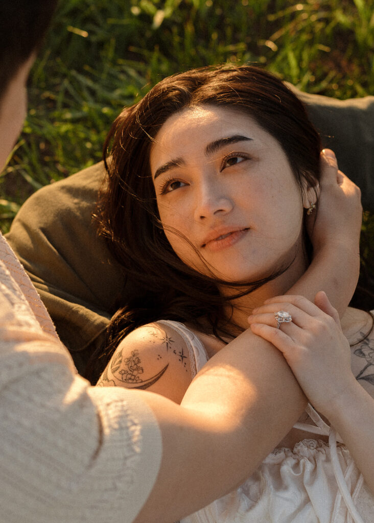 Woman lying in grass gazing lovingly at her partner, showing her engagement ring