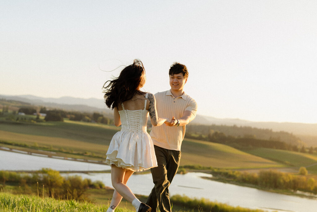 Couple running hand in hand across a hillside at golden hour