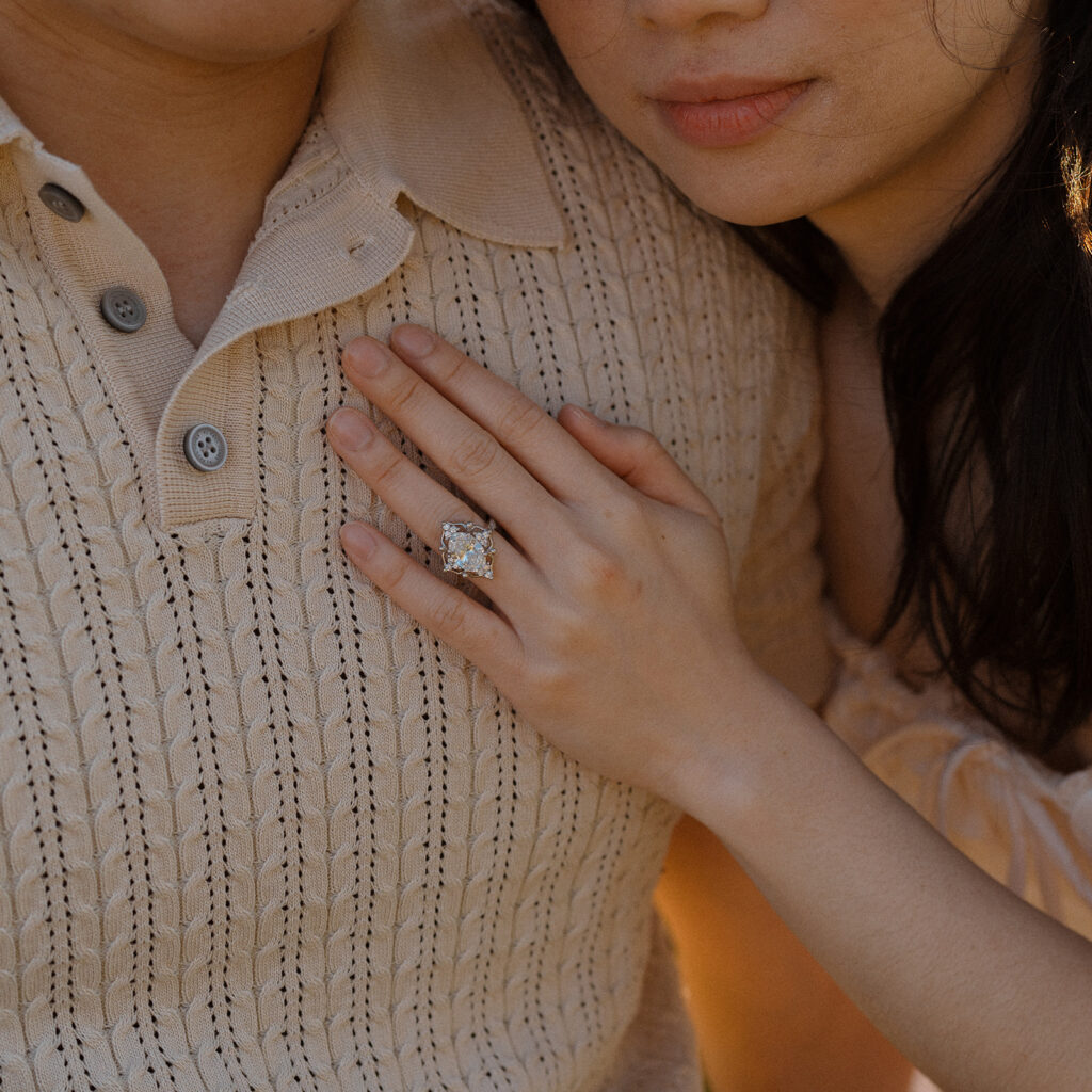 Woman resting her hand with engagement ring on her partner’s chest
