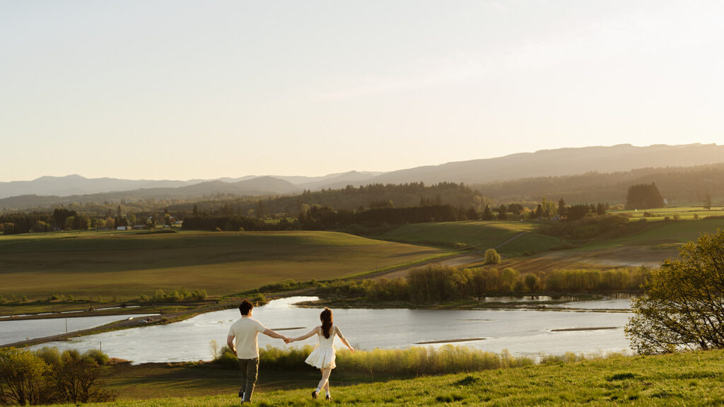 Couple holding hands walking toward a scenic lake view at sunset
