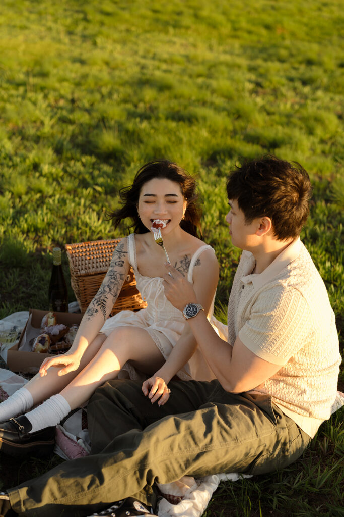 Couple enjoying a picnic as the woman takes a bite from a fork offered by her partner