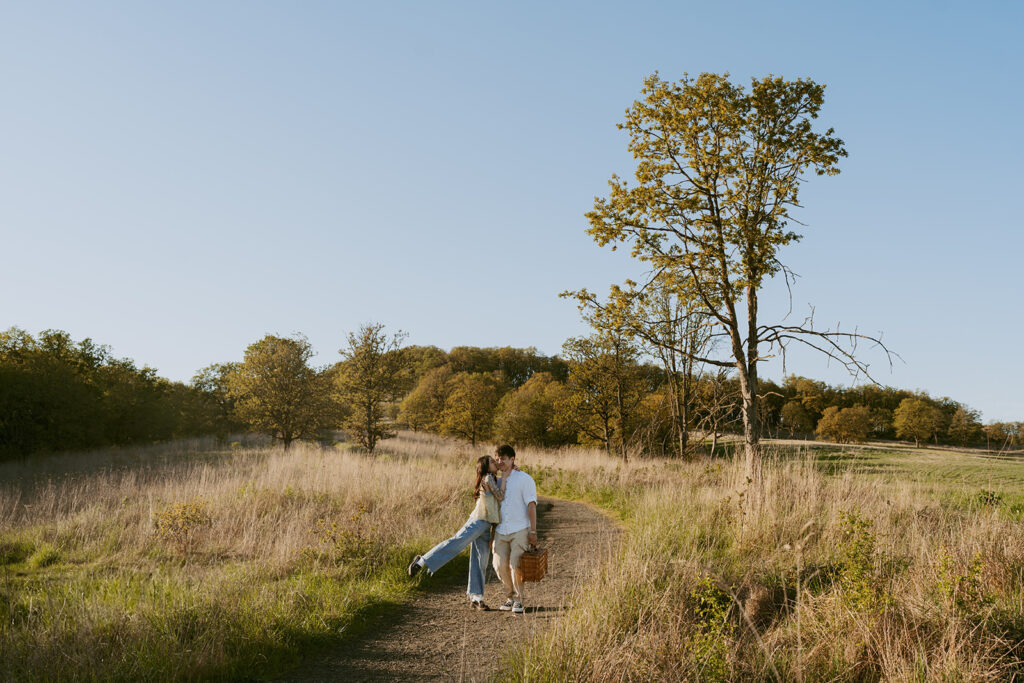 Couple kissing on a nature trail, carrying a picnic basket