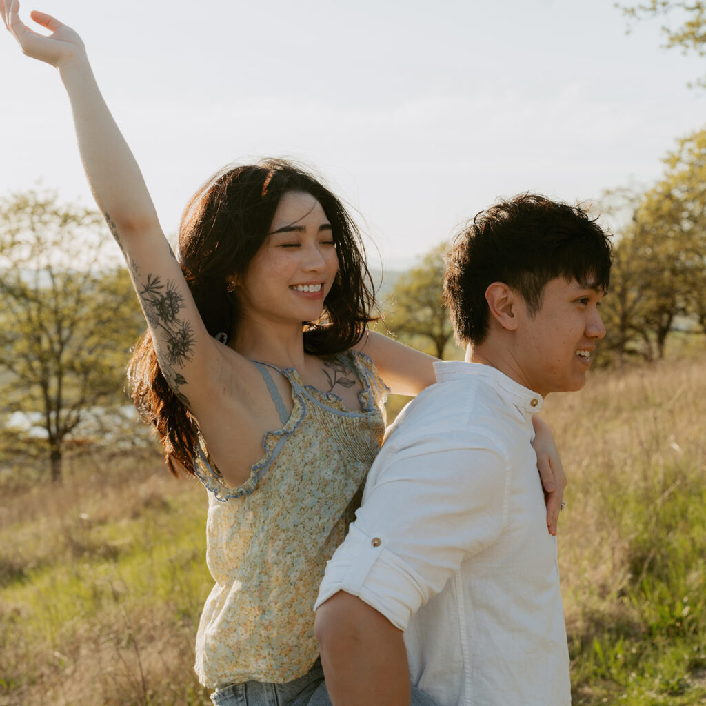 Woman raising her arms joyfully while riding on her partner’s back