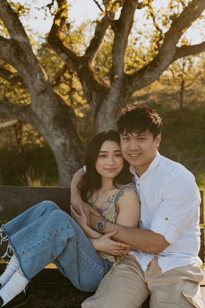 Couple sitting close together on a bench under a tree