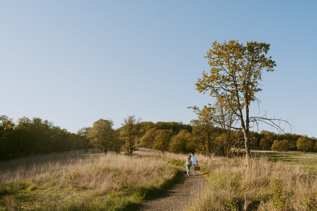 Couple walking hand in hand down a trail with a picnic basket