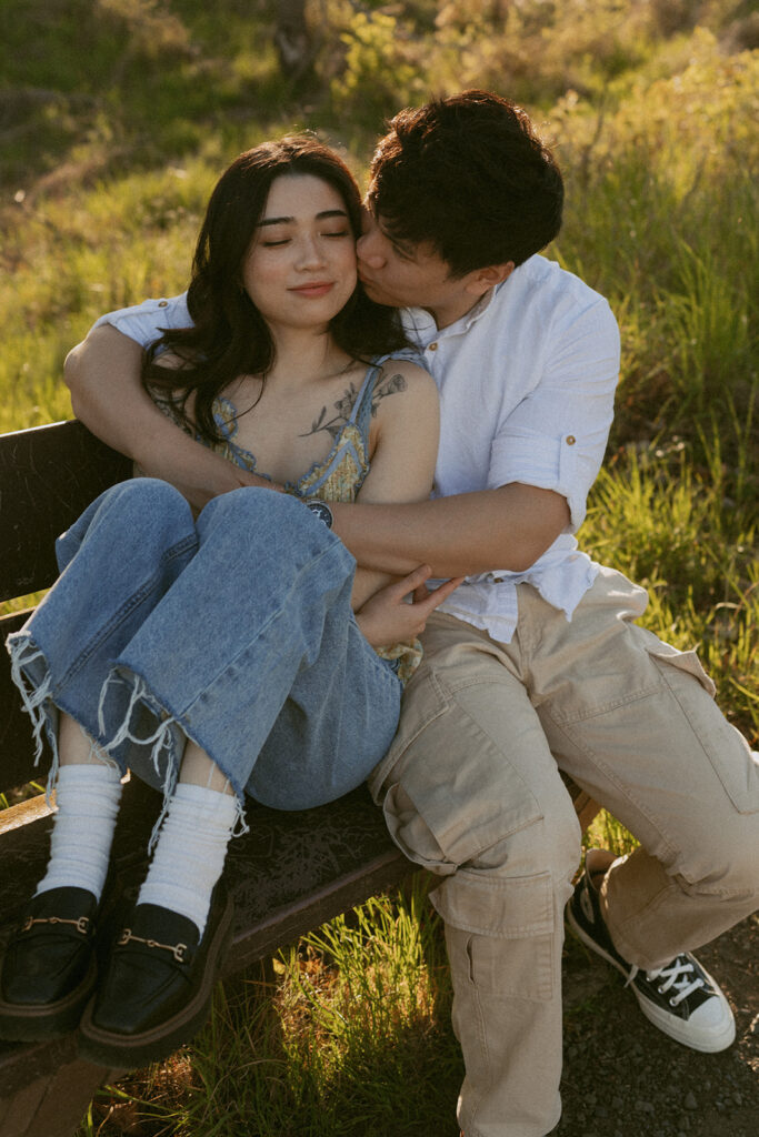Man kissing his partner's cheek as they cuddle on a bench