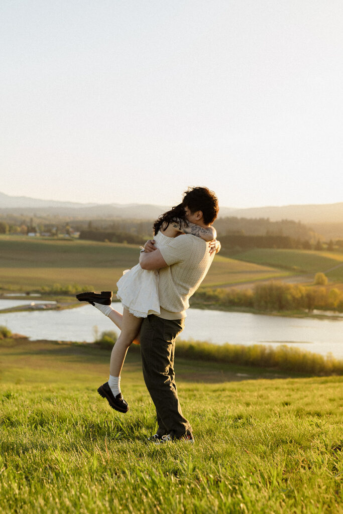 Man lifting and embracing his fiancée in a grassy field