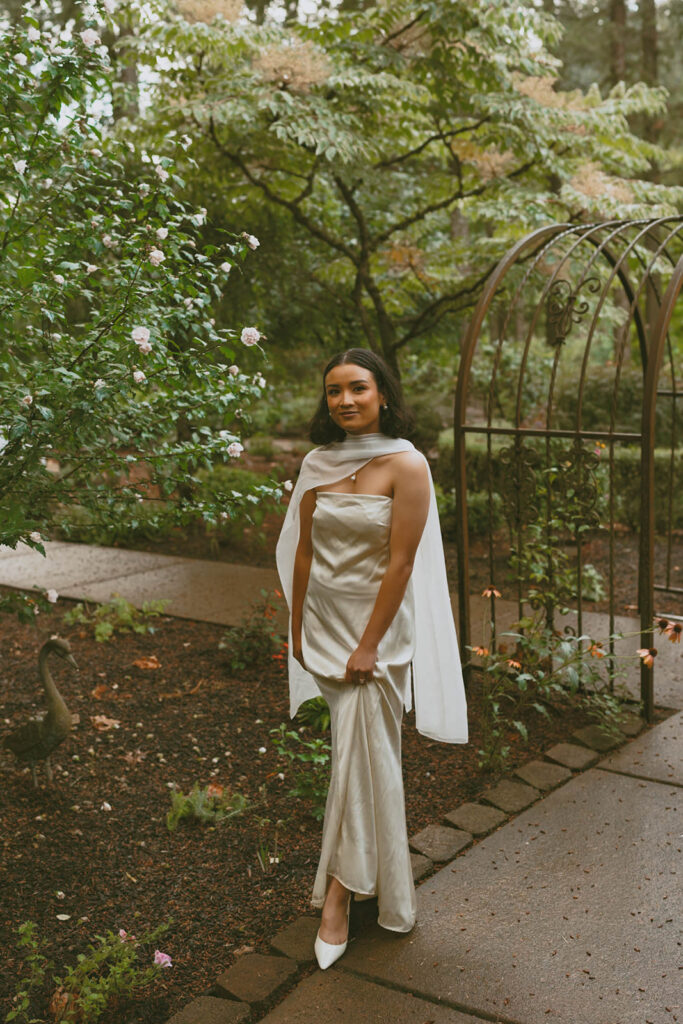 Bride poses alone in a garden wearing a satin gown