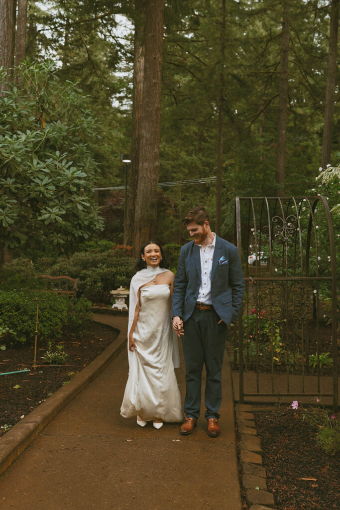Bride and groom walk hand in hand, smiling in a lush garden