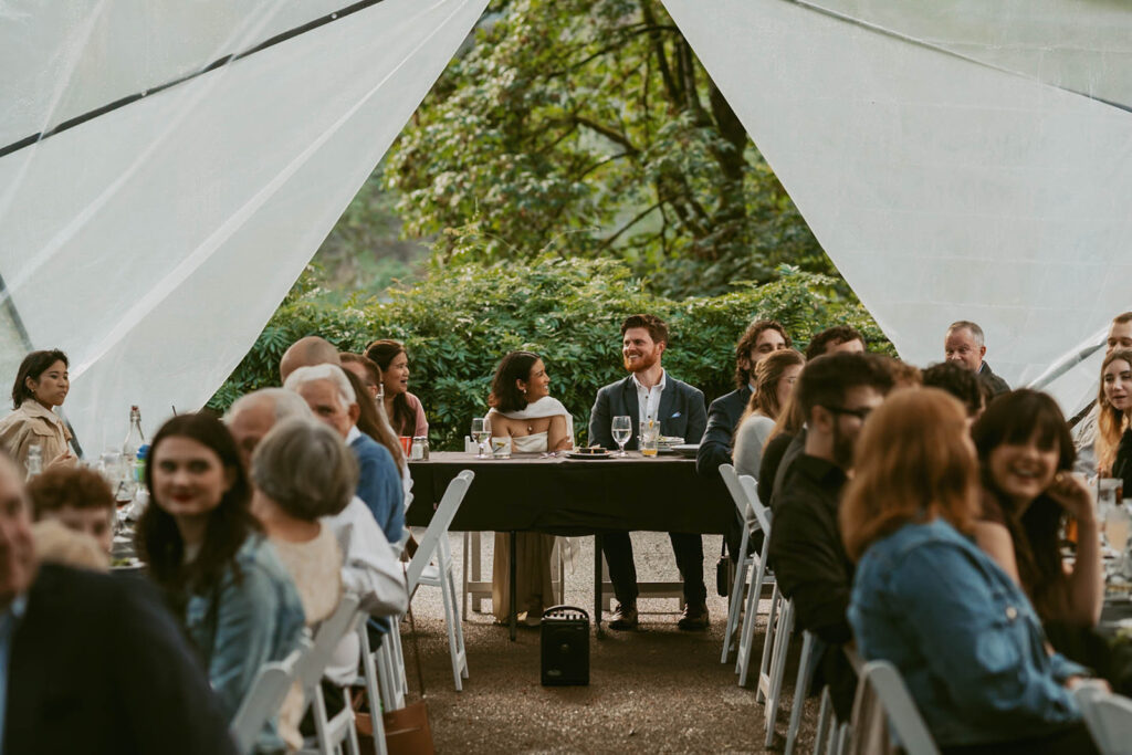 Guests dine under a clear tent during a wedding rehearsal