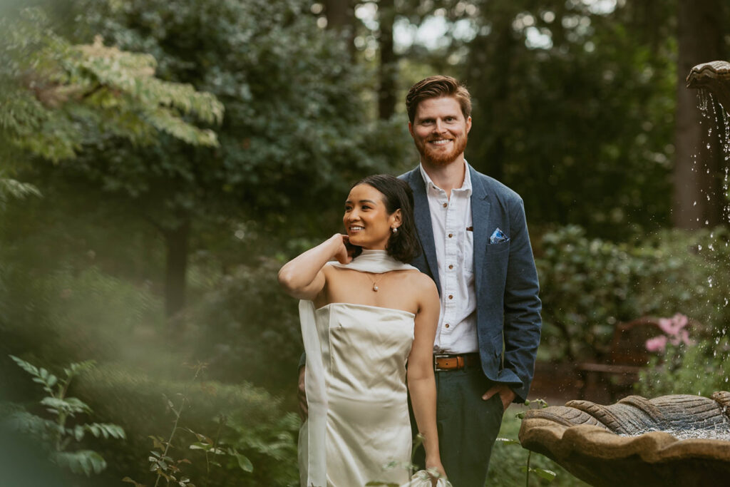 Couple poses smiling next to a garden fountain