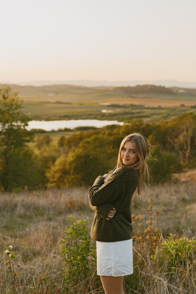 Woman in a green sweater looking over her shoulder with a scenic valley behind