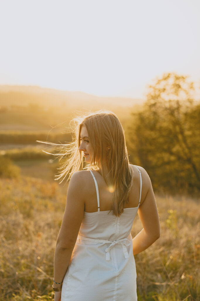 Back view of a woman in a white dress standing in a glowing field at golden hour