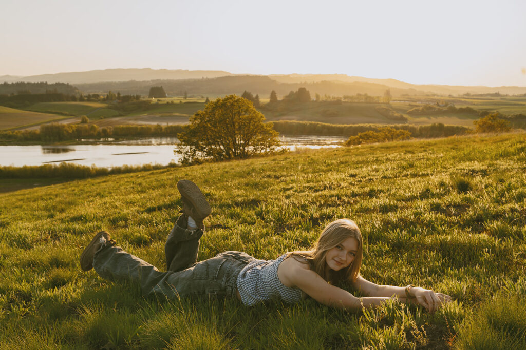 Woman laying on her stomach in a green field, smiling with a sunset view