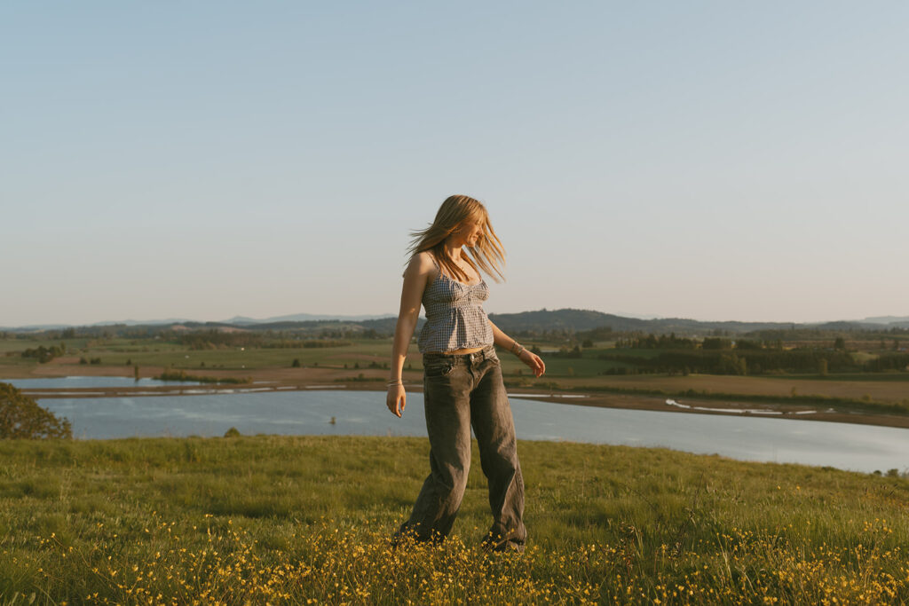 Girl twirling in a field with lake and hills in the background