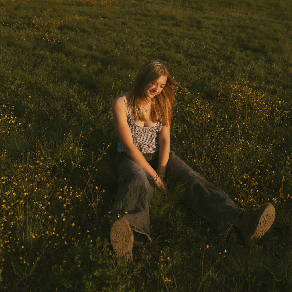 Girl sitting in grass surrounded by yellow wildflowers