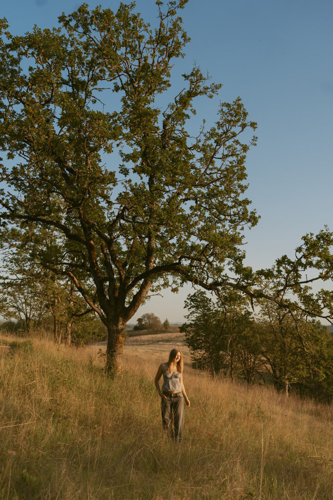 Girl walking under a large tree in a grassy field