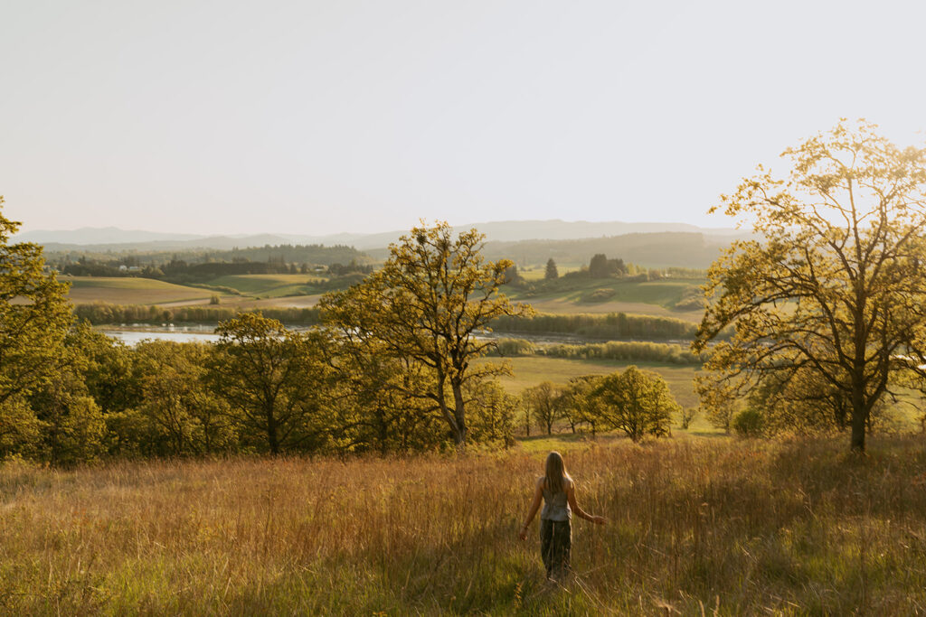Woman walking alone on a hillside surrounded by trees at sunset