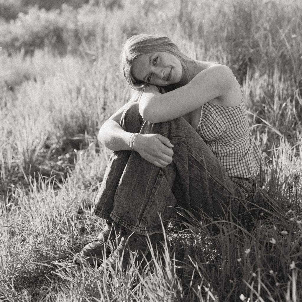Girl sitting in tall grass, resting her head on her knees, black and white