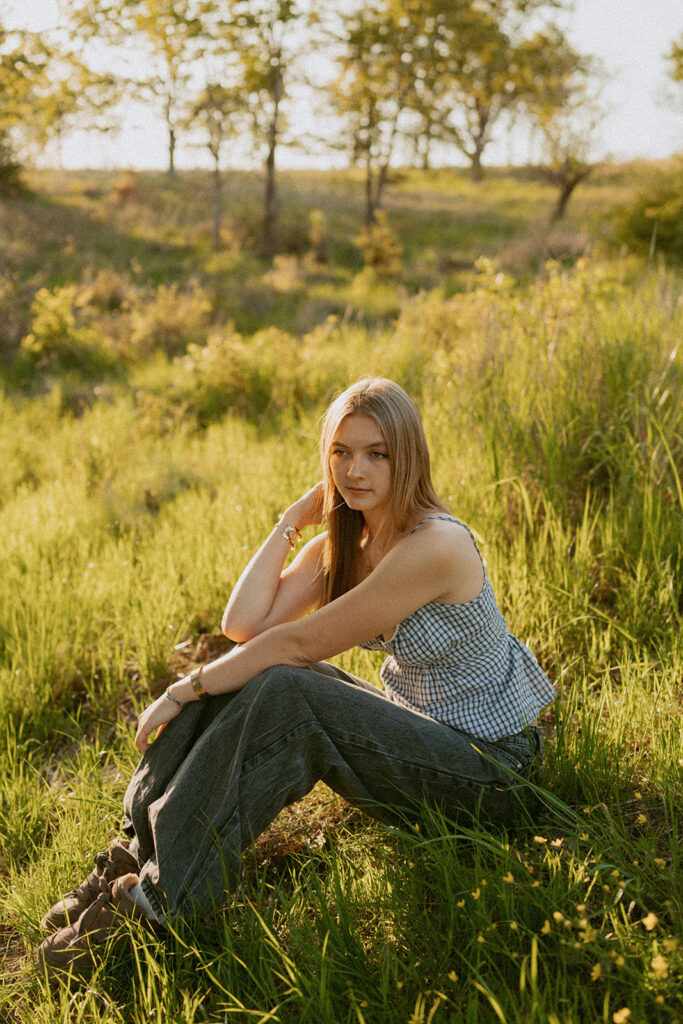 Girl sitting in sunlit grass, looking off to the side