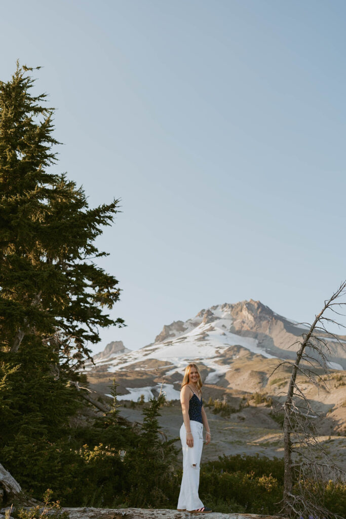 A woman is standing in a field with a mountain in the background.