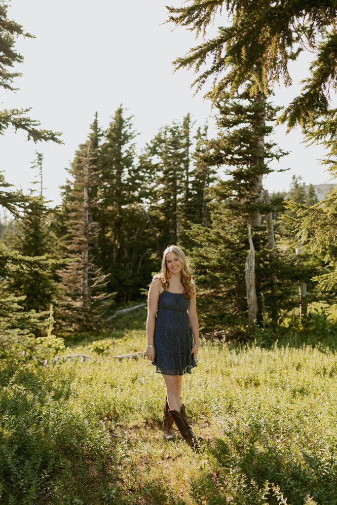 A woman in a blue dress is standing in a field surrounded by trees.