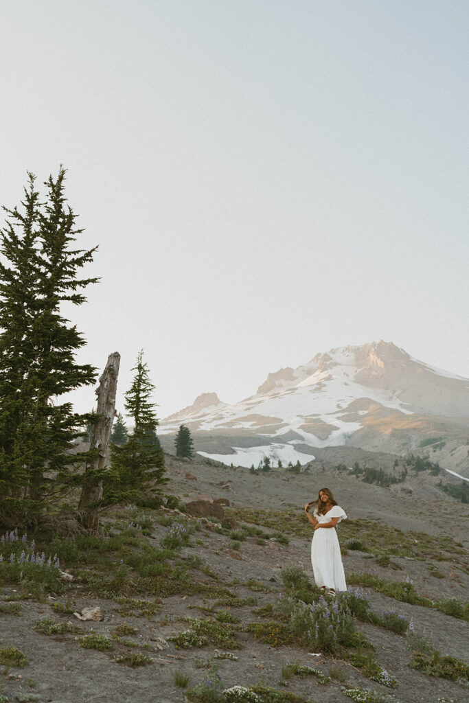 A woman in a white dress is standing on top of a mountain.