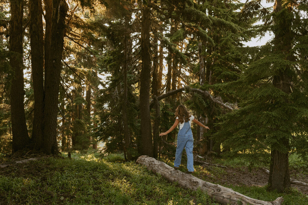 A person is standing on a log in the middle of a forest.