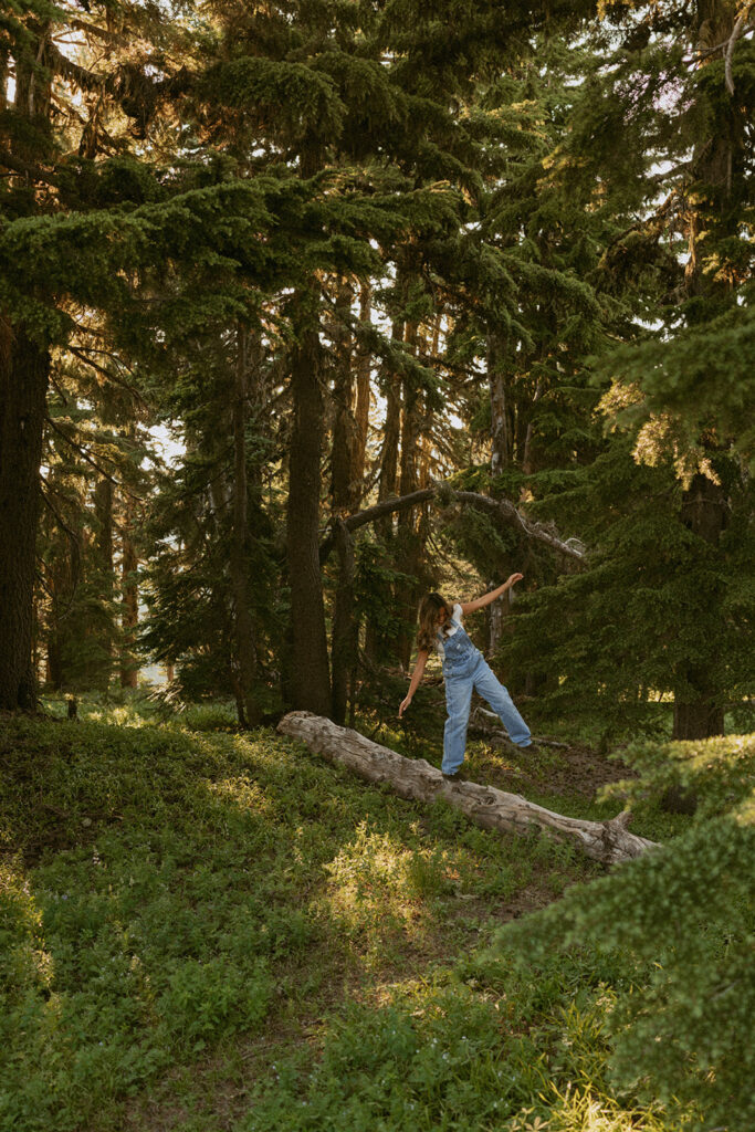A person is standing on a log in the middle of a forest.
