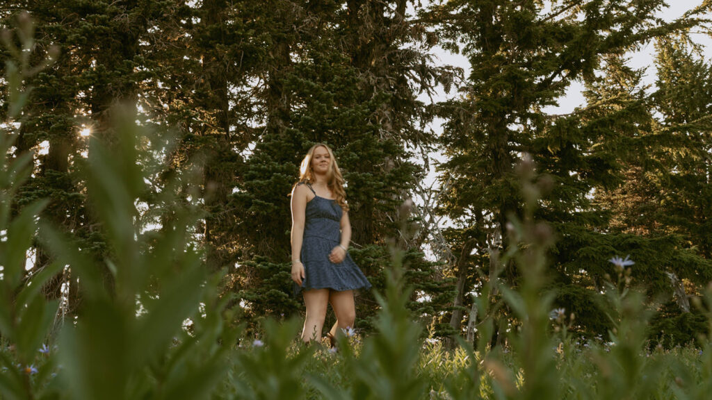 A woman in a blue dress is standing in a field in the woods.