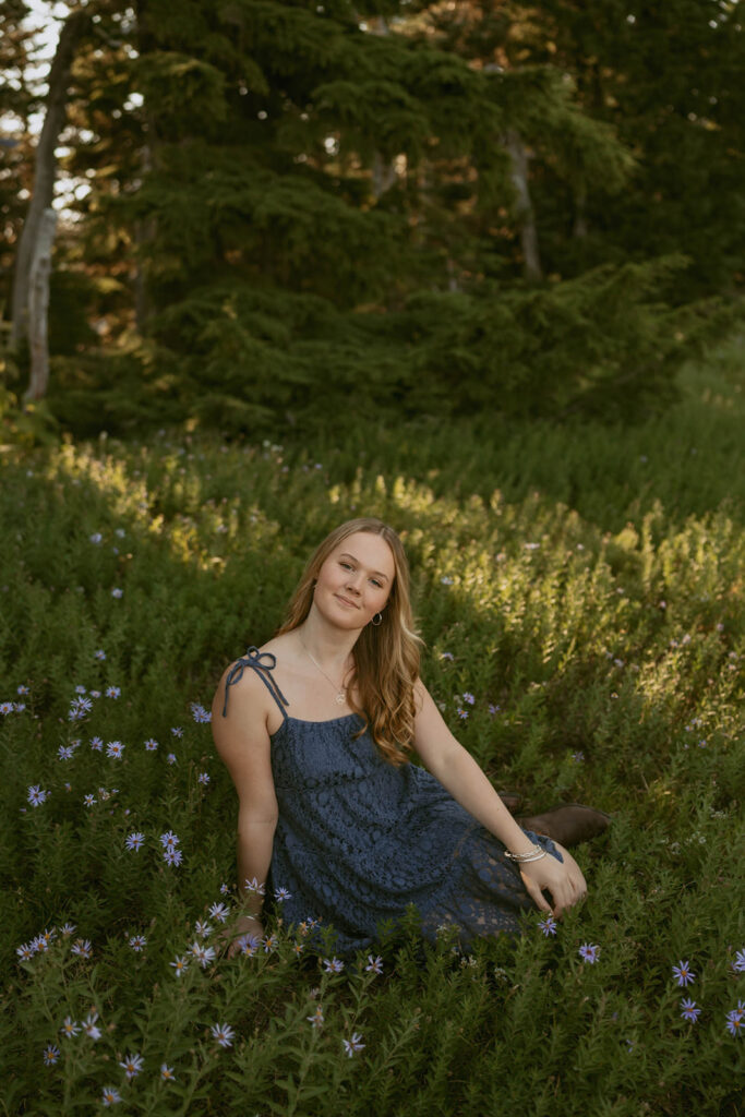 A woman in a blue dress is sitting in a field of flowers.