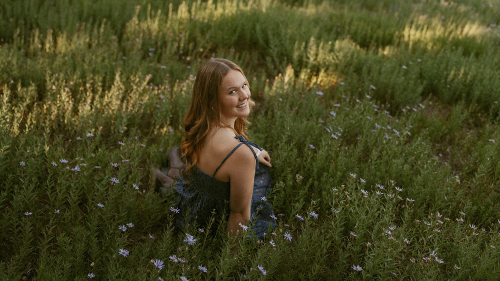 A woman in dress is sitting in a field of flowers.