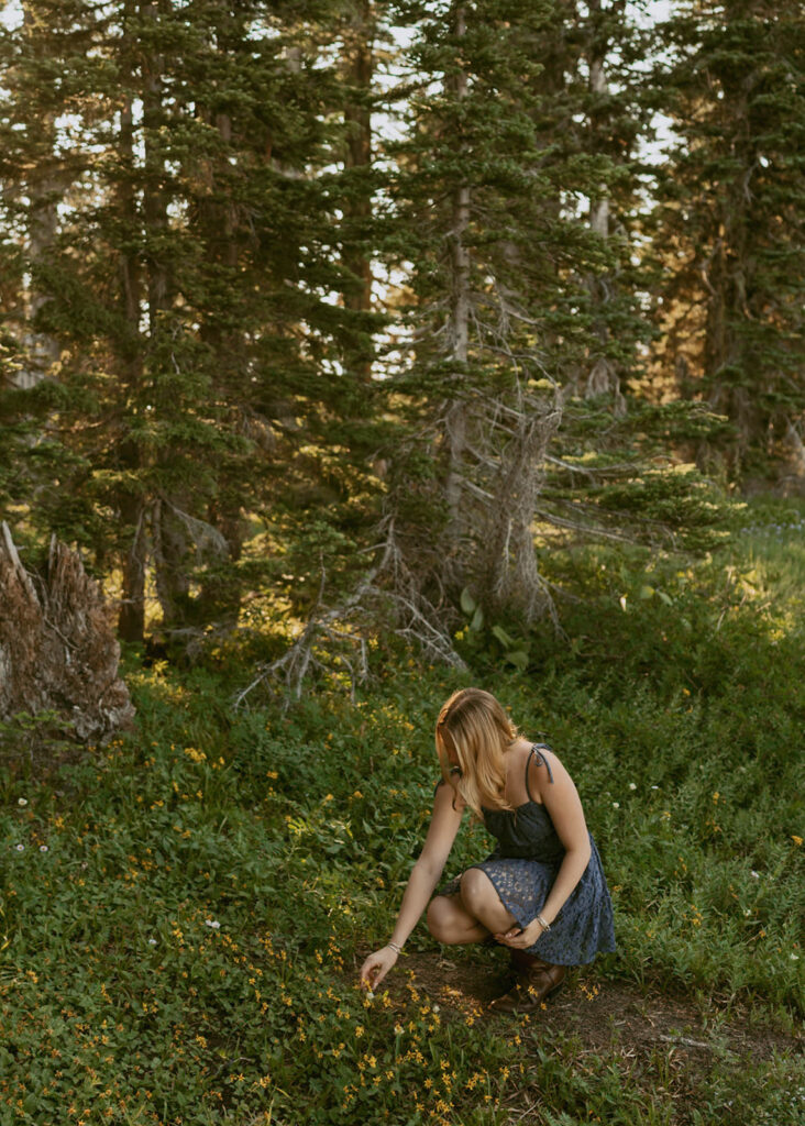 A woman is picking flowers in the woods.