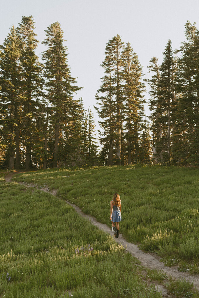 A woman is walking down a path in a field surrounded by trees.