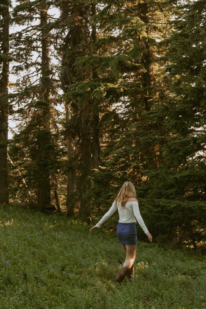 A woman is walking through a grassy field in the woods.