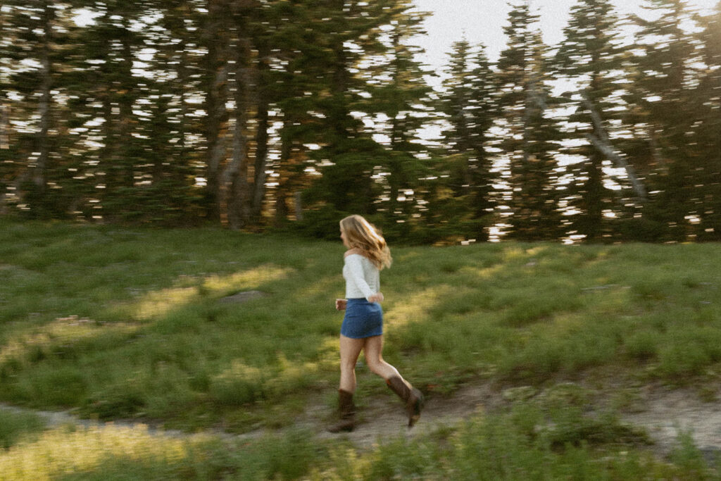 A woman is walking through a grassy field with trees in the background.