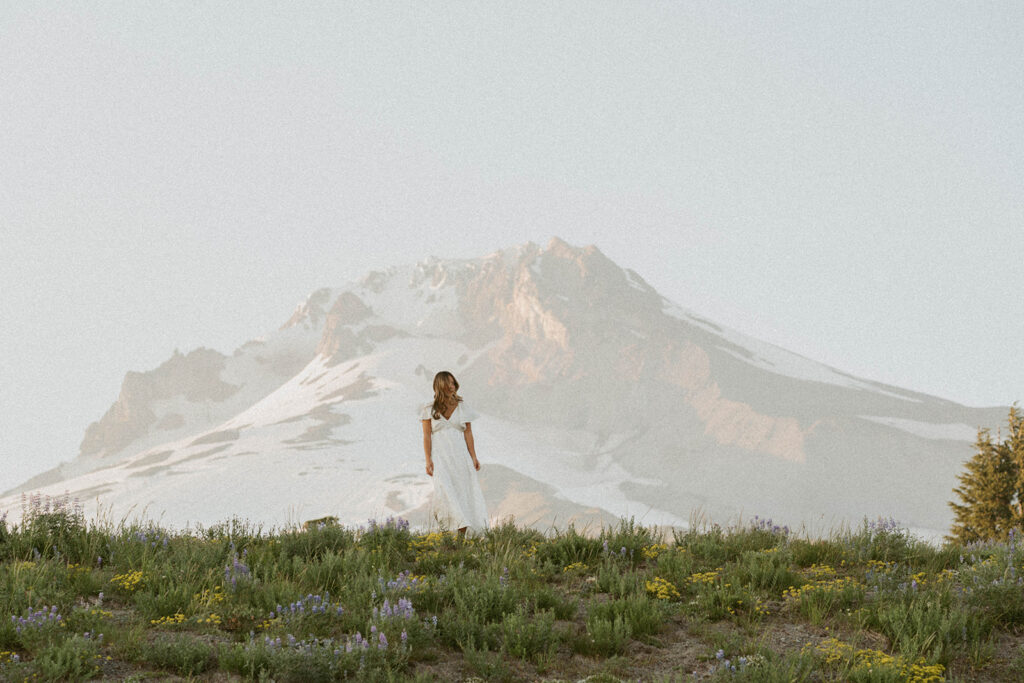A woman in a white dress is standing in front of a mountain.