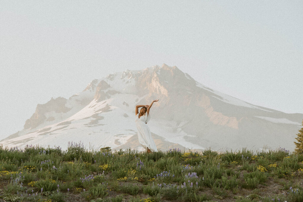 A woman in a white dress is standing in front of a mountain.