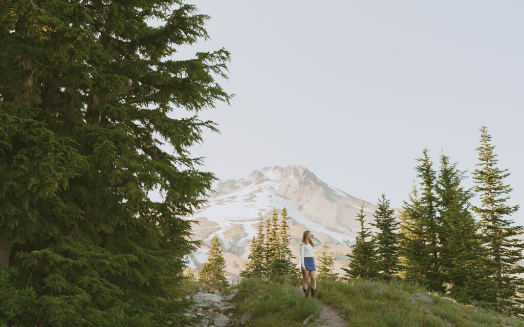 A woman is standing on top of a mountain surrounded by trees.