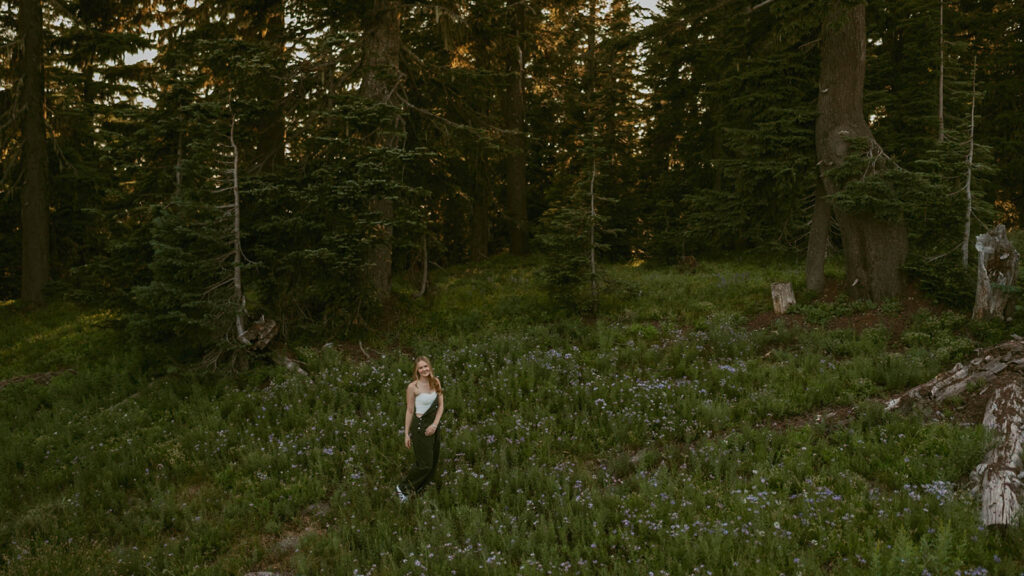 A woman is standing in a field of flowers in the woods.