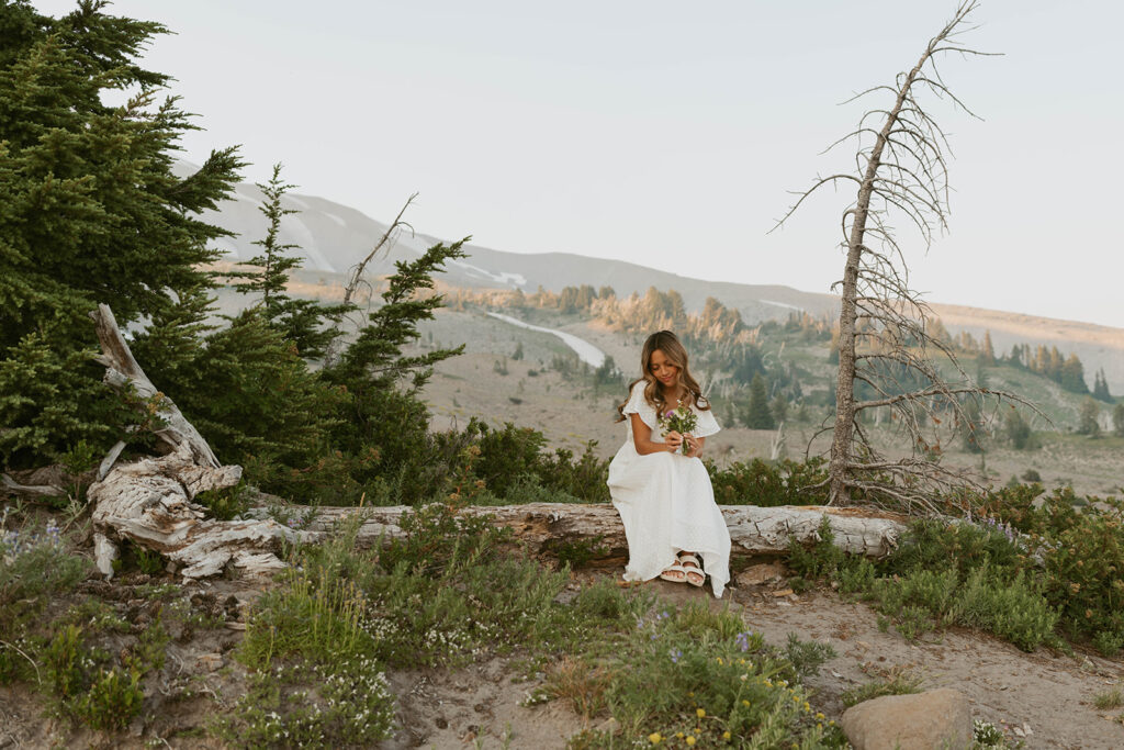 A woman in dress is sitting on a log in the woods.