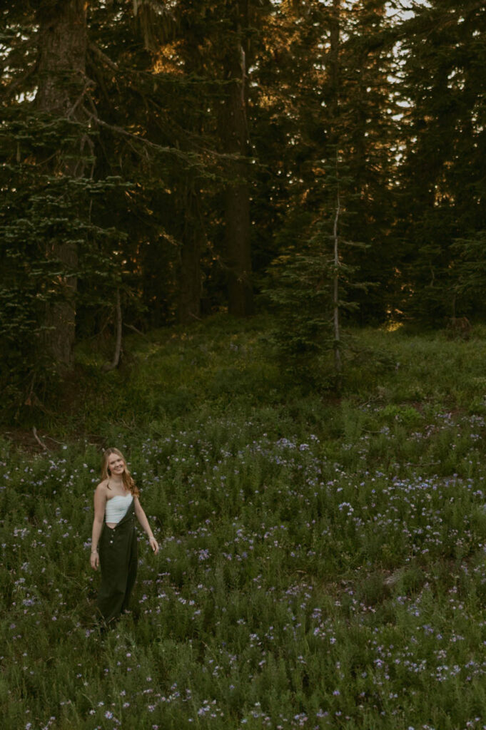 A woman is standing in a field of flowers in the woods.