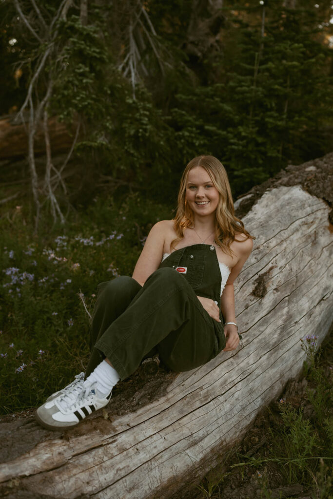 A woman is sitting on a log in the middle of a forest.