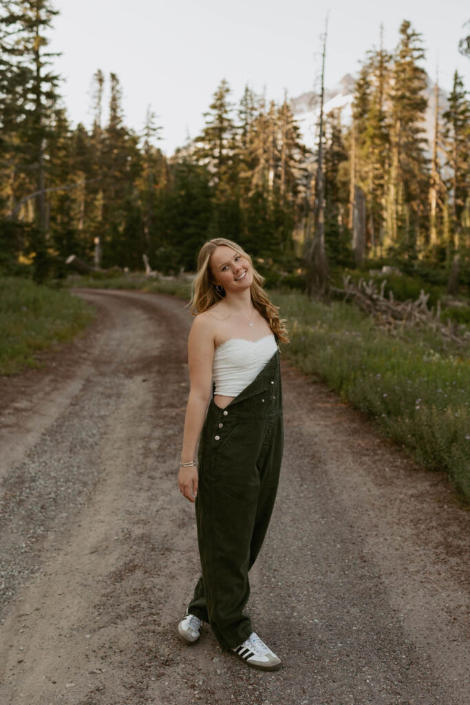 A woman in overalls is standing on a dirt road.